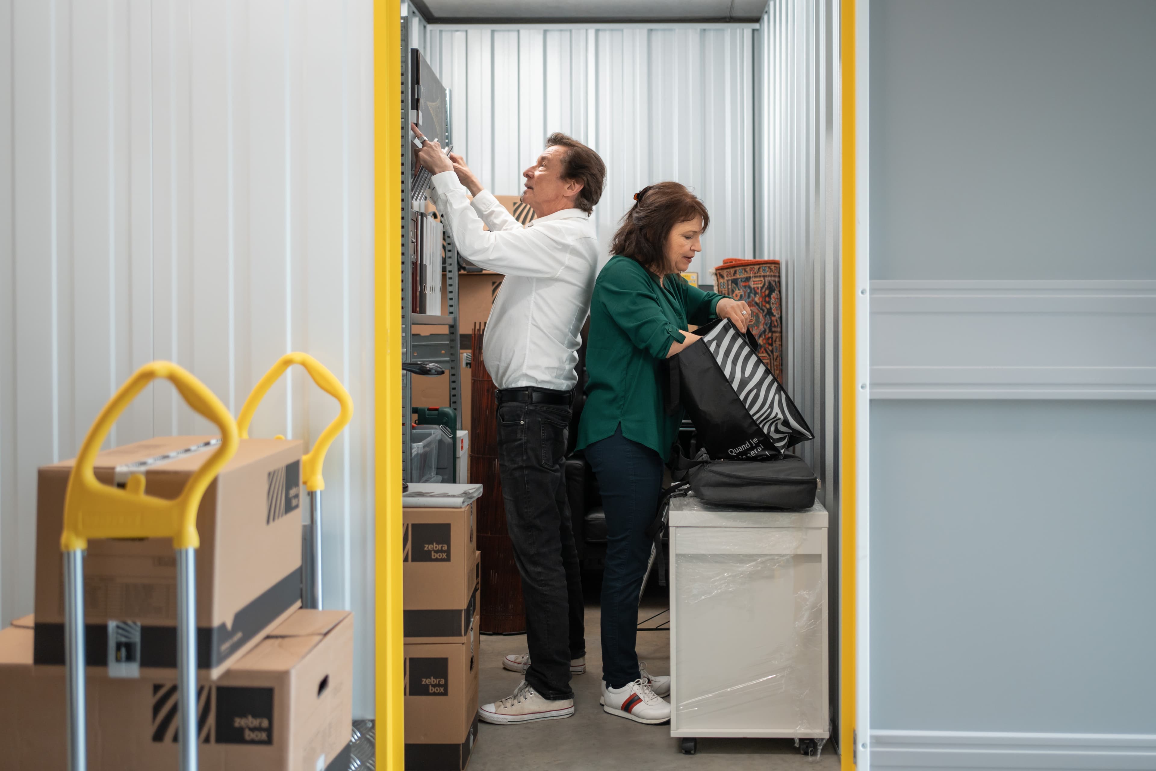An elderly couple is standing back to back looking at stored items in their storage unit at Zebrabox.
