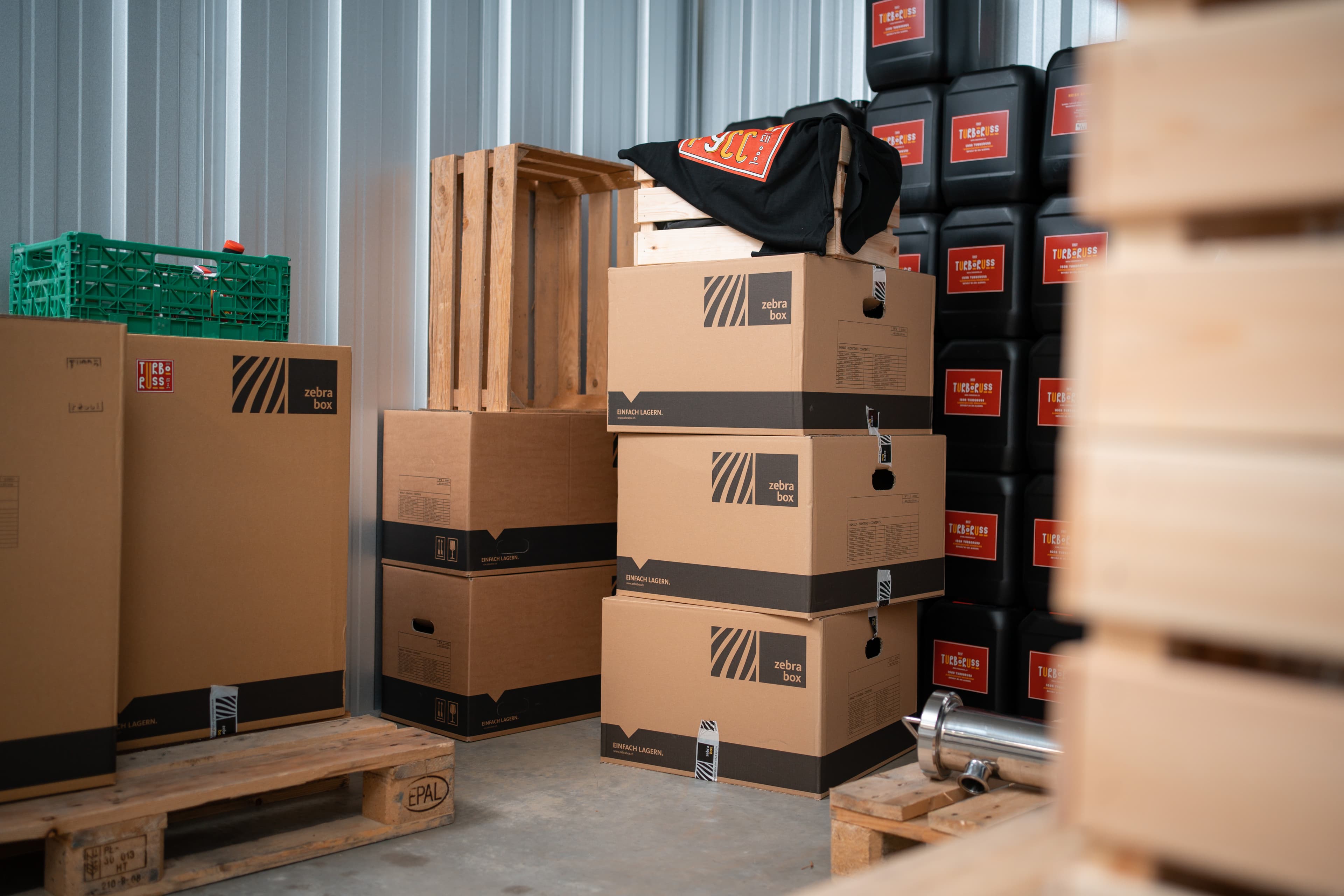 In a Zebrabox storage unit, a company's warehouse is visible with beverage cans, wooden crates, moving boxes and wooden pallets.